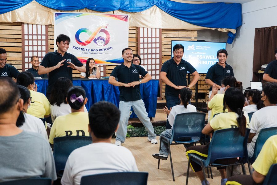 Foundation staff in navy shirts stand at the front of a chapel facing seated mothers and children.